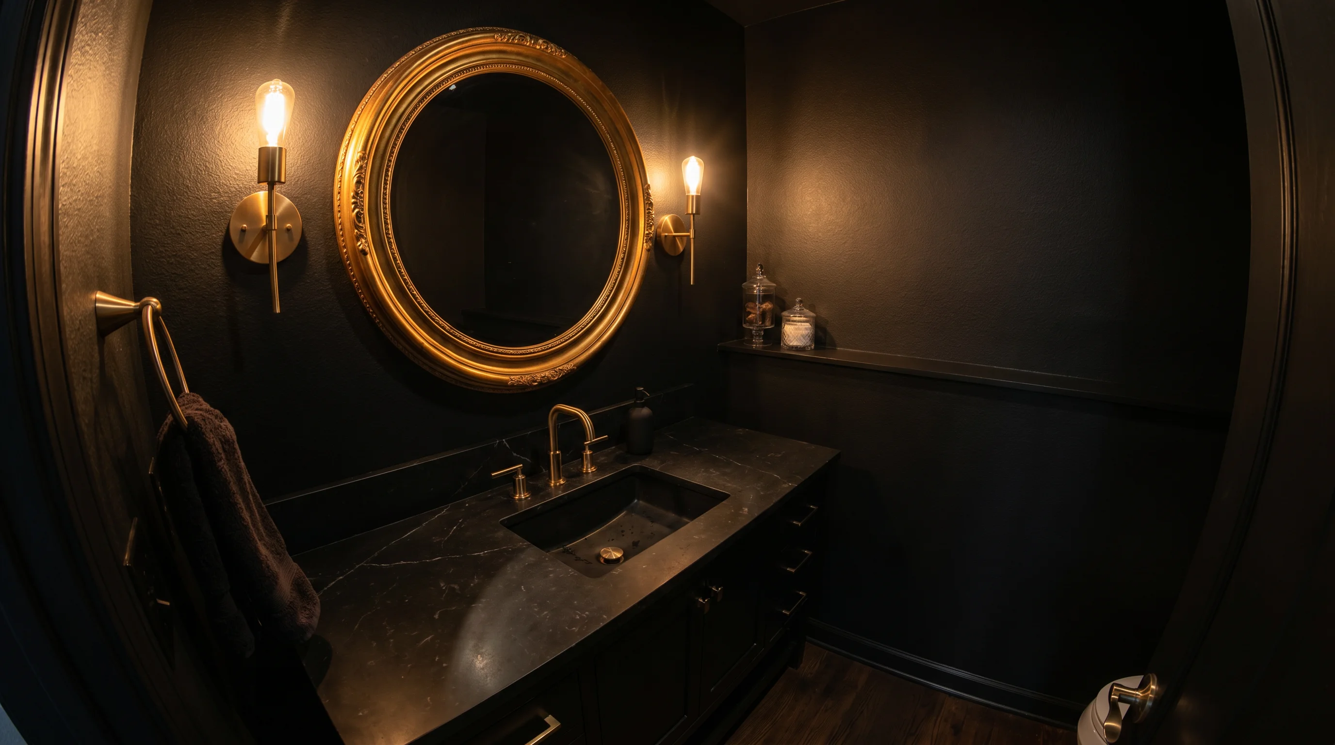 A dramatic powder room drenched in matte black with a bold statement mirror, brushed gold faucet and sconces, and a black stone vanity — a jewel-box guest bathroom