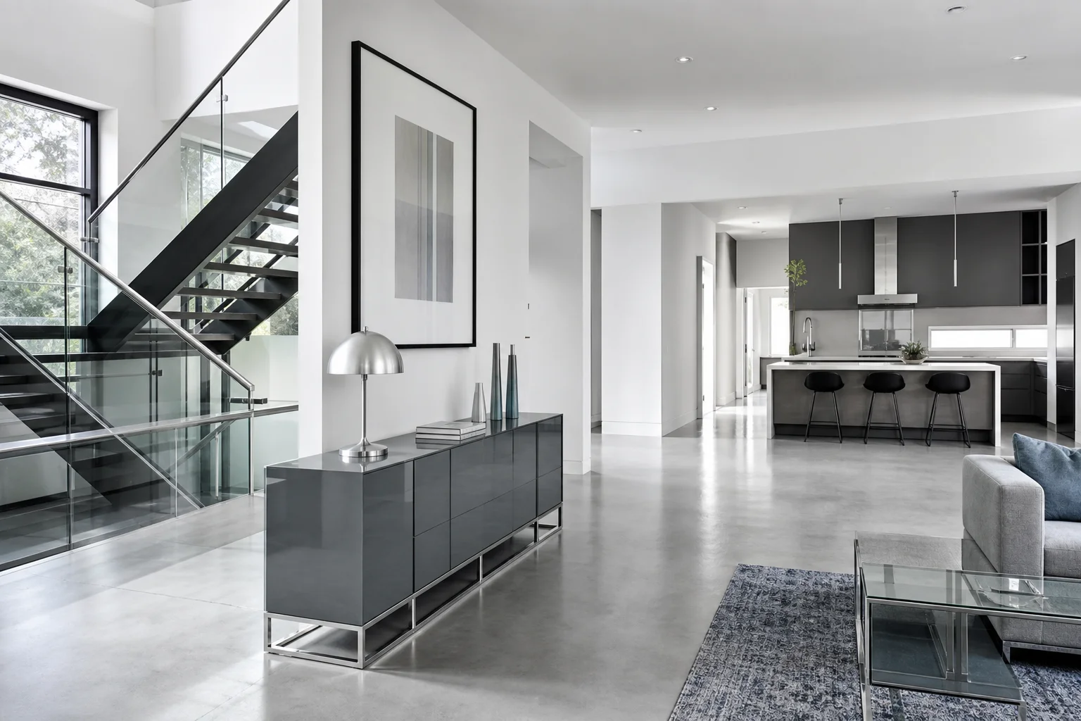 A cool-toned minimalist living room with white walls, a light gray sofa, polished concrete floor, glass coffee table and chrome accents, bright daylight