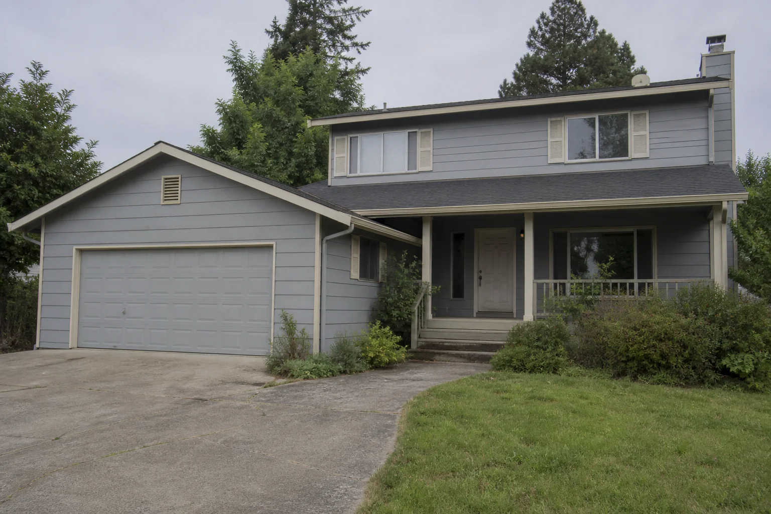 Side-by-side before and after of the same suburban house — left painted a dated cool gray with overgrown beds, right repainted a warm khaki neutral with white trim, a sage-green front door and tidy landscaping